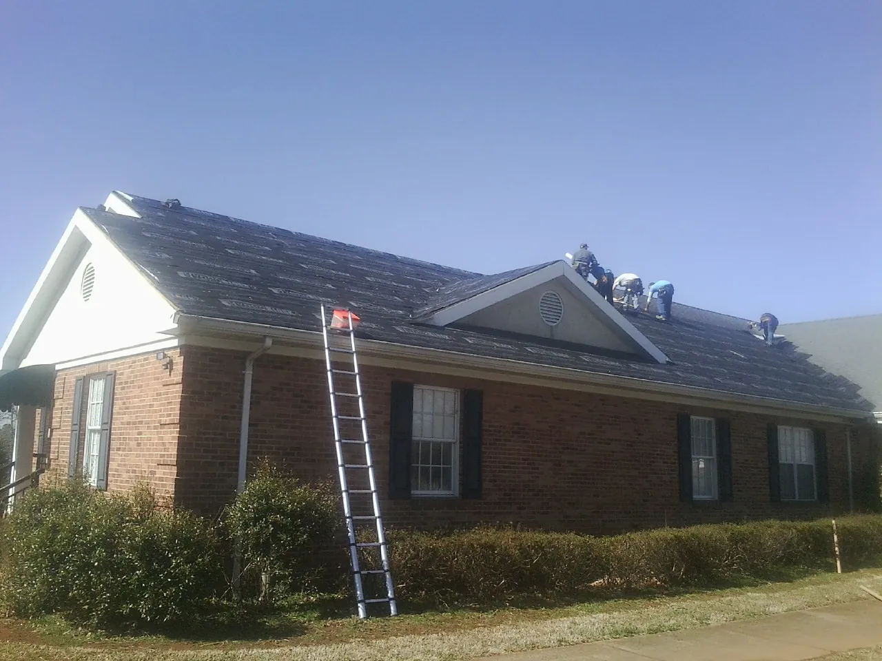 Crew tearing shingles off a brick ranch roof with a ladder set — Emergency Roof Repair work by our crew in Bantry