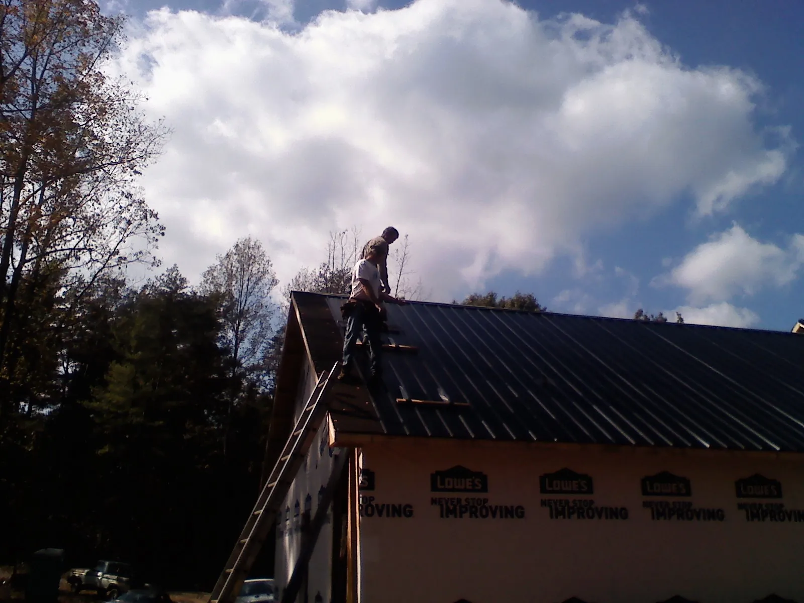 Roofer fastening dark metal panels high against a cloudy sky, from a Roof Inspection job in Bantry
